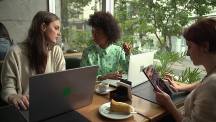 Young women working in front of laptop computer at coffee shop exchanging ideas. Female entrepreneurs using technology - Powered by Adobe