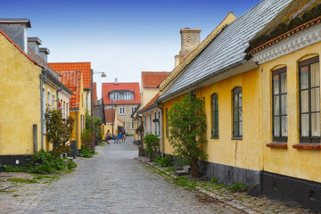 Fototapeta na wymiar Old yellow houses located in Dragoer, Denmark. Tiny ancient houses in historical city. Alleys with yellow painted houses, red roofs, and cobblestone streets built in the traditional Danish style