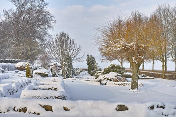 Frosted cemetery and frozen trees in winter fall. Foggy snowy cemetery, grave stones and trees covered in the winter snow. Landscape of a graveyard covered with snow on a wintery day in Denmark. - Powered by Adobe