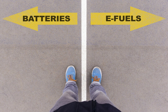 Batteries or E-Fuels choice, text on asphalt ground, feet and shoes on floor