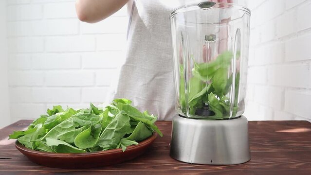 Women's hands shift fresh spinach into a blender for making smoothies The concept of healthy eating.