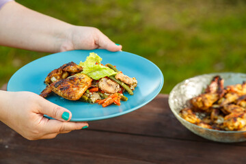 Female hands put a plate with chicken and vegetables on the table next to a dish with grilled chicken.