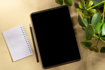 A tablet and notepad for writing on a beige background with leaves and shadows. Template for business layout. Top view, flat lay