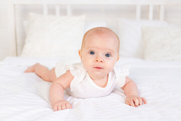 baby girl smiles lying on her stomach on a white cotton bed at home