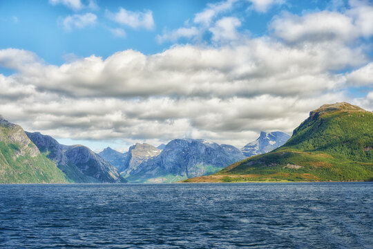 Landscape of mountains north of polar and arctic circle in Bodo, Norway. Scenic view of green hills surrounded by ocean in remote area with clouds. Traveling abroad, overseas for holiday and vacation