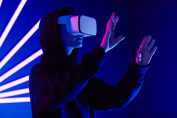 Futuristic shot of young woman wearing VR headset in 3 dimensions with neon light beams , copy space