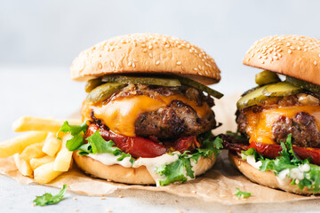 Delicious craft cheeseburgers with roasted pepper, cheddar cheese and dill pickles served with french fries. Light grey stone background