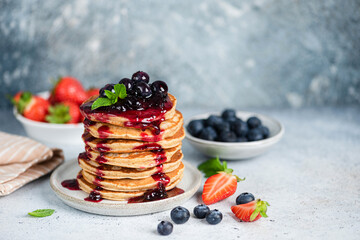 Pancakes with berry fruit preserves topping over blue concrete background. Copy space for text or design elements. Sweet breakfast pancakes stack with jam