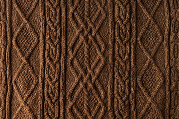 Knitted brown background. Large knitted fabric with a pattern. Close-up of a knitted blanket