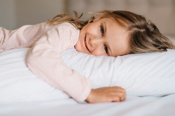 Happy smiling child girl lying on the bed on white fluffy pillow good morning enjoy new day