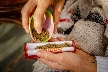 Sao Paulo, SP, Brazil - June 26 2022: Female hands preparing cigarette with cannabis flower using gourd and baller details.