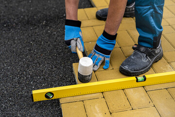 The hand of the worker using a rubber hammer and water-level for aligns the interlocking paving stone.