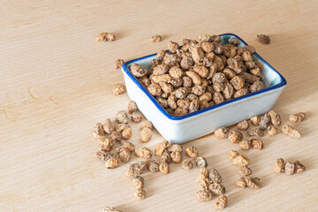 Overflowing container with dried and natural tiger nuts, on wooden table.