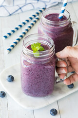 Hand holding a jar mug of fresh blueberry smoothie with another in behind.