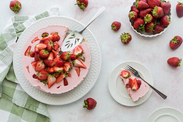A fresh homemade strawberry cheesecake with one serving on a plate to the side.