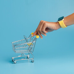 a woman's hand rolls a miniature cart from a supermarket. the concept of shopping. blue background