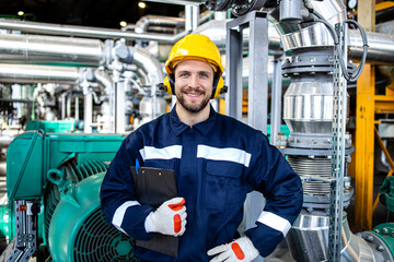 Portrait of professional refinery engineer standing in oil and gas production plant. In background pipeline and pumps.