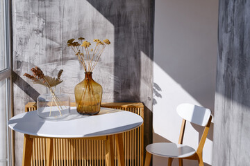 Ornamental dry grass flowers  in glass vases on a white table with morning sunlight on a gray background © Iuliia Pilipeichenko
