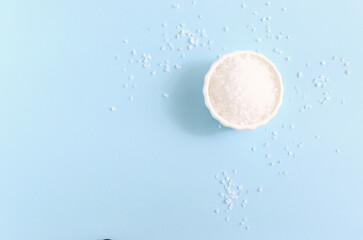 Sea coarse salt in a white ceramic bowl on a blue background. Natural resource. Salt is suitable for cooking and beauty treatments. Horizontal orientation. Copy space. Top view