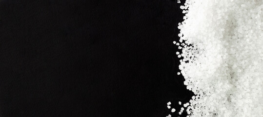 Banner. Black background, sprinkled with white sea salt. Rough texture. Salt is suitable for cooking and beauty treatments. Horizontal orientation. Top view. copy space