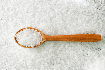 Background from white sea salt with a wooden spoon. Rustic style. Rough texture. Salt is suitable...