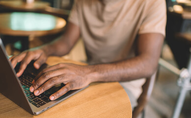 Cropped dark skinned male typing on laptop computer working on online project browsing websites, skilled software programmer communicating in social networks while creating web design via netbook app