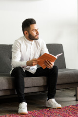 Young man reading a book on his sofa. charismatic and intelligent entrepreneur. Colombian person smiling being in her house. security and self-confidence. network marketing worker