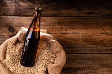A bottle of dark beer in a bag of wheat. A beam of light falls on a bottle of beer. View from above. - obrazy, fototapety, plakaty