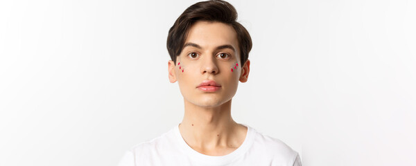 People, lgbtq and beauty concept. Close-up of beautiful androgynous man with glitter on face, looking at camera, standing over white background - Powered by Adobe