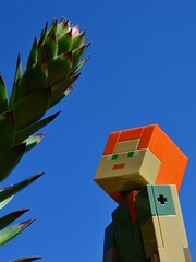 Fototapeta premium LEGO Minecraft large figure of Alex examining huge tall stem of succulent Sempervivum plant, also called houseleek, blue summer skies in background.