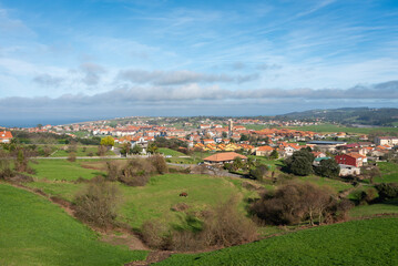 Fototapeta na wymiar Beautiful top view of the picturesque town of Ajo surrounded by green fields under a blue sky crowded by clouds, Cantabria, Spain