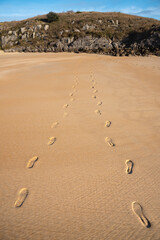 Footprints in the sand of a beach towards a small mountain