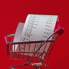 Einkaufswagen mit Kassenbon vor rotem Hintergrund