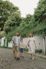 Fototapeta na wymiar Father, mother and son are holding hands on the green cobbled street of an old European town. Happy family in the evening. Tourists at sunset.