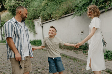 Father, mother, and smiling son are holding hands on the green cobbled street of an old European town. Happy family in the evening. Tourists at sunset.