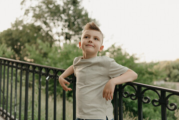 The close portrait of a boy near the iron stair railing on the green street of an old European town. Happy fellow in the evening. Young tourist at sunset.