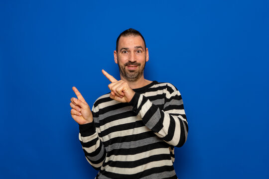 Happy smiling 40 year old man in ryas sweater pointing with index fingers to the side at mock up workspace area isolated on blue color background studio portrait. People lifestyle concept.