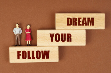 On a brown surface, wooden blocks with the inscription - FOLLOW YOUR DREAM, there are figures of...