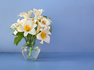 Bouquet white flowers lilies in glass vase on a blue table with space for text