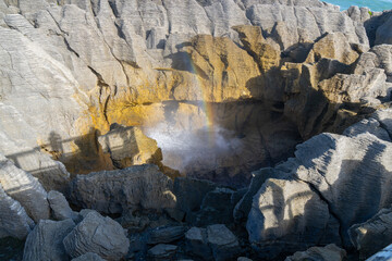 Deep hole in stratified layers of rock through which sea surges causing spray