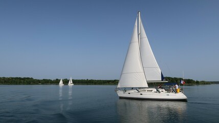 Fototapeta premium Nautisme sur le lac du Der Chantecoq, en Champagne Ardenne, dans la région Grand Est, avec un voilier blanc naviguant sur l’eau bleue du lac (France)