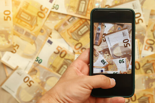 man hand takes a picture of euro banknotes on smartphone. Money paper 50 euro banknotes on the background of a smartphone screen, the concept of business, investment and income growth.
