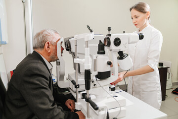 Naklejka na ściany i meble doctor examines elderly man's eye on screen of autorefractometer. 