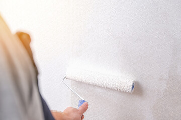 A man is painting vinyl wallpaper with a velour roller for painting with white paint. Renovation of the room.
