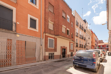 Fototapeta na wymiar Narrow street with low buildings with clay brick facades with balconies and terraces and cars parked on the road