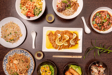 Fototapeta na wymiar Set of Asian dishes seen from above, lemon breaded chicken fillets, three delights rice, stir-fried noodles, spring rolls, takoyaki, pork ramen and poke bowl