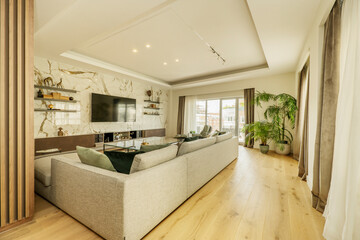 TV room with beige fabric sofas, marble clad wall and window with drawn curtains and exit to the terrace with plants in a corner of the room