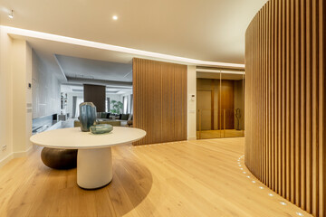 Hallway of luxury home with round table with vases, slatted walls and oak floorboards