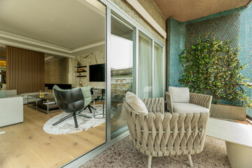 Terrace with gray fabric armchairs, blue wall with vertical garden and access to a living room with aluminum window