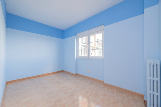 Empty room with light brown stoneware floors, cast iron radiator and walls painted in two shades of blue